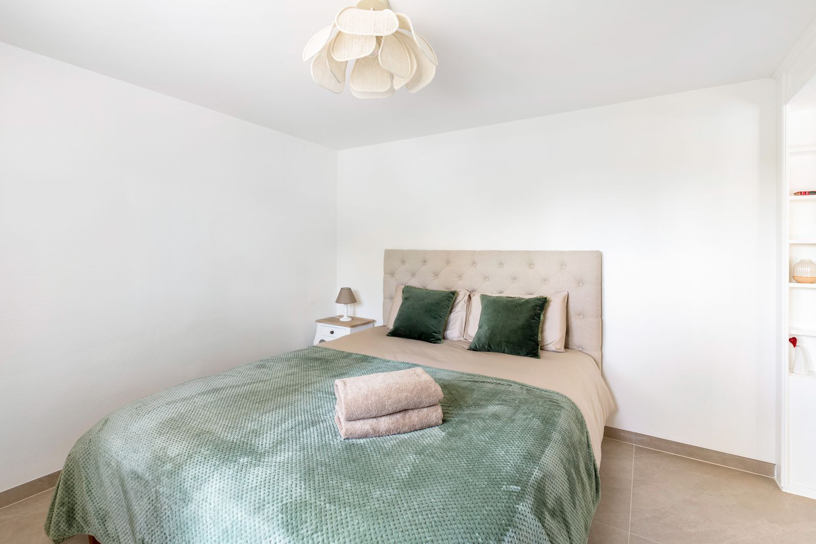 Chambre au lit capitonné, plaid vert sauge et coussins en velours