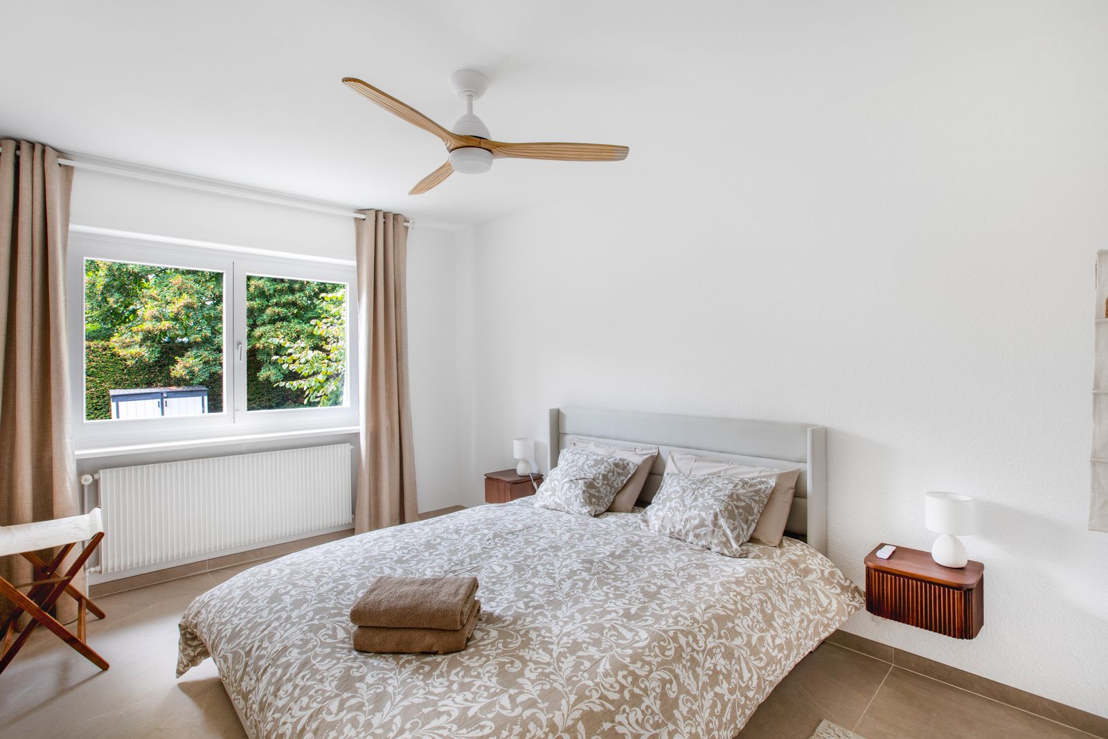 Chambre avec ventilateur de plafond, lit et tables de chevet en bois