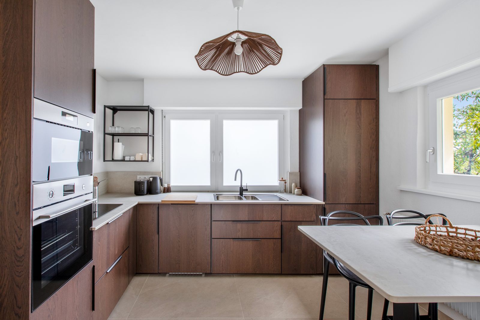La cuisine en bois sombre, plan de travail clair et table haute avec tabourets