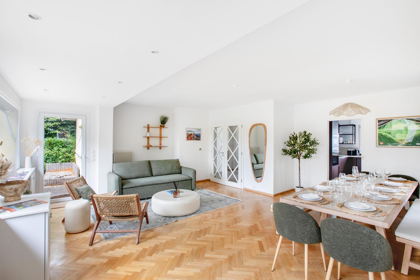 La pièce de vie : canapé vert sauge, fauteuils en rotin et grande table dressée sous les fenêtres